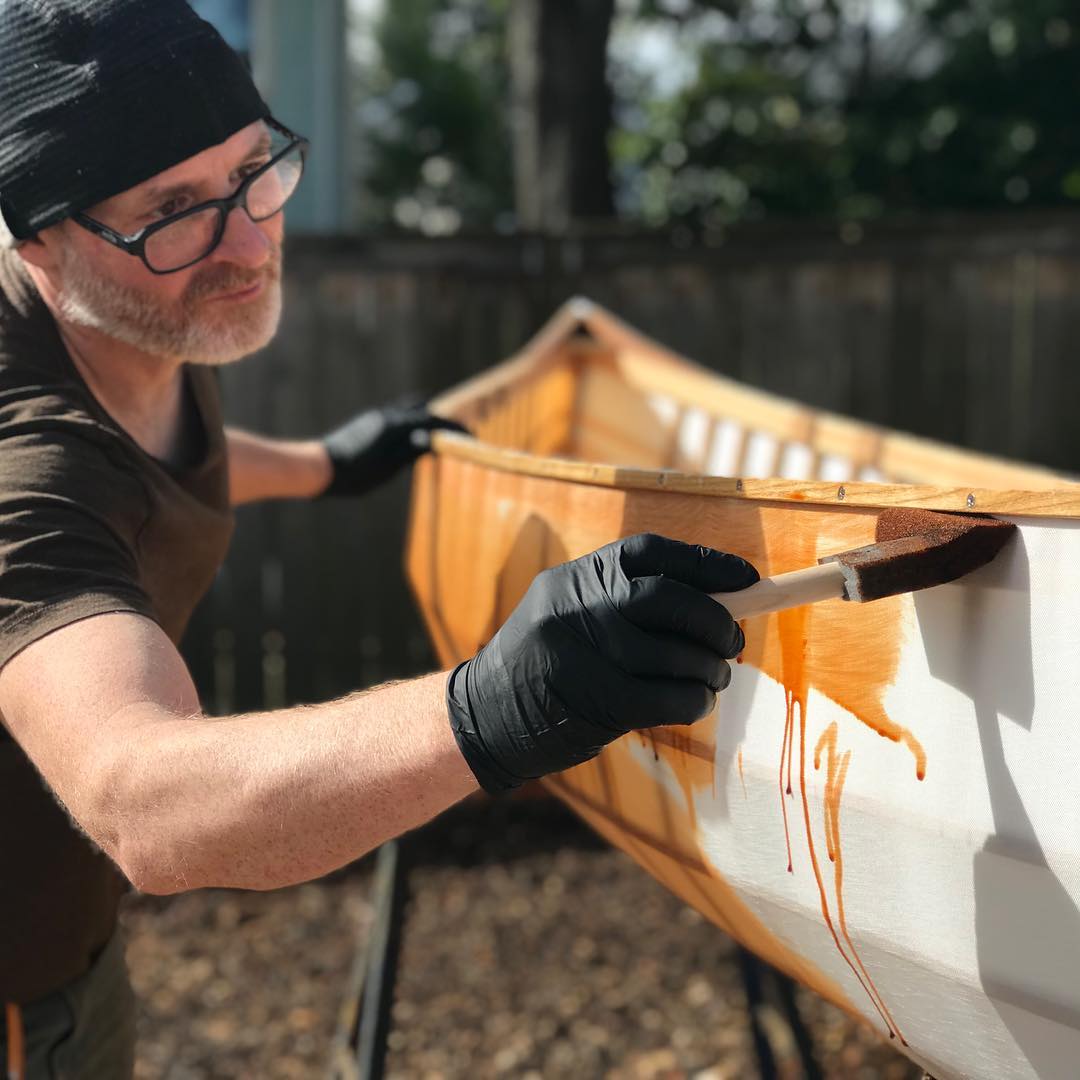 Man dyeing a skin on frame canoe orange using acid dye