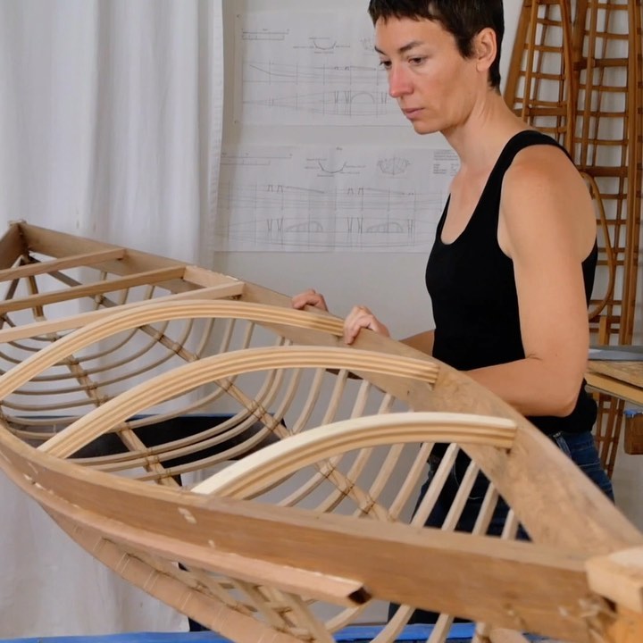 woman standing next to partially completed kayak frame