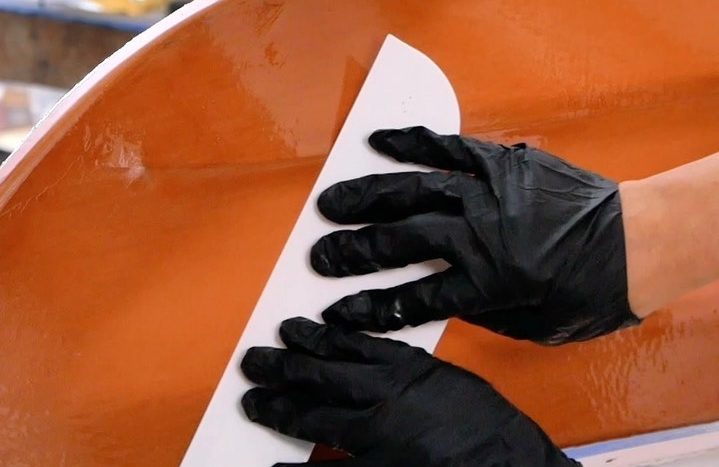 hands holding a plastic squeegee and smoothing the finish on the kayak skin