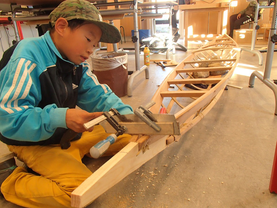 east greenlandic boy sawing the bow of a traditional skin on frame kayak
