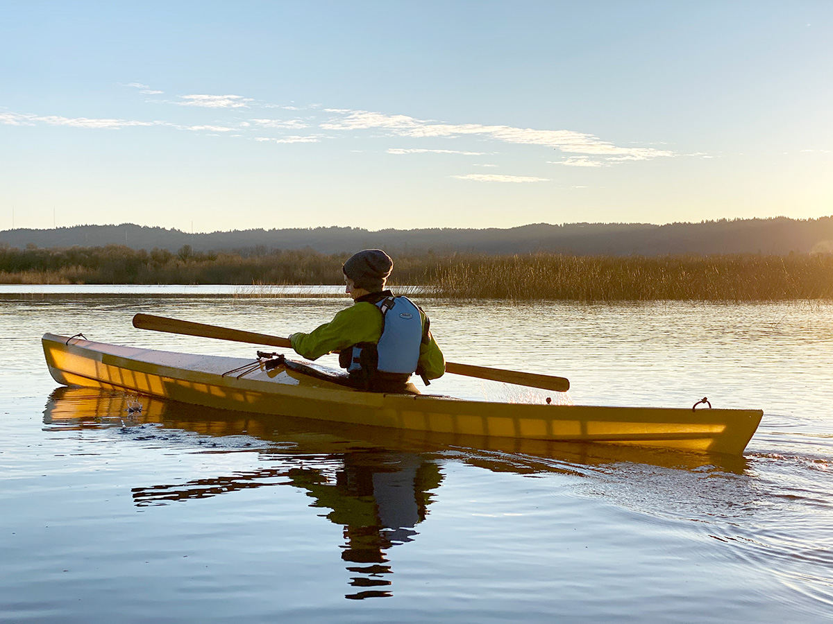 kayaker paddling a modern skin on frame LPB kayak backlit by the sun