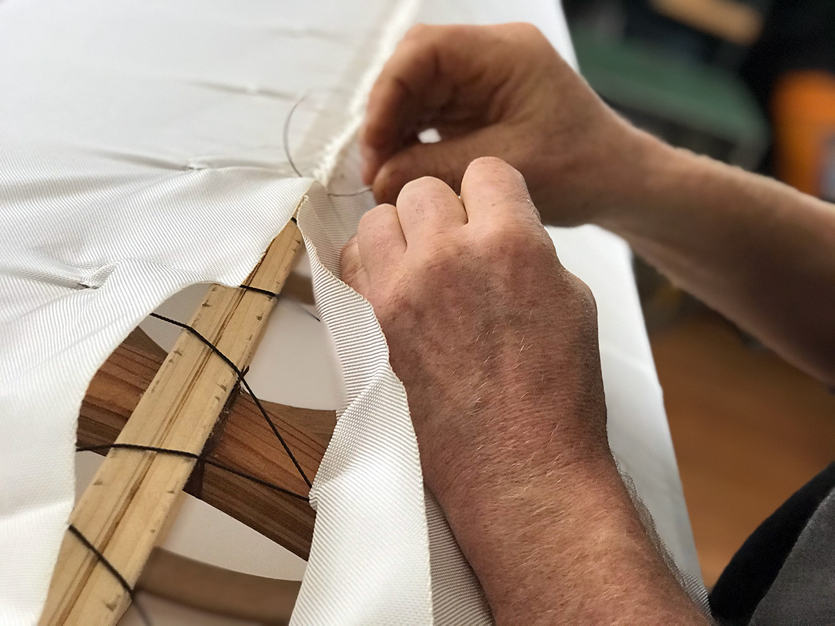 close up of hands stitching a nylon skin closed around a kayak frame