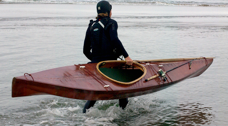 Kayaker carrying a Cape Falcon F1 kayak in one hand into the ocean
